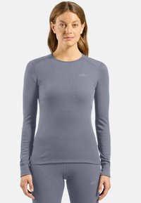 Long-sleeve top in light gray, made from ribbed fabric. Features rounded neckline and subtle brand logo on the chest, fitted design.