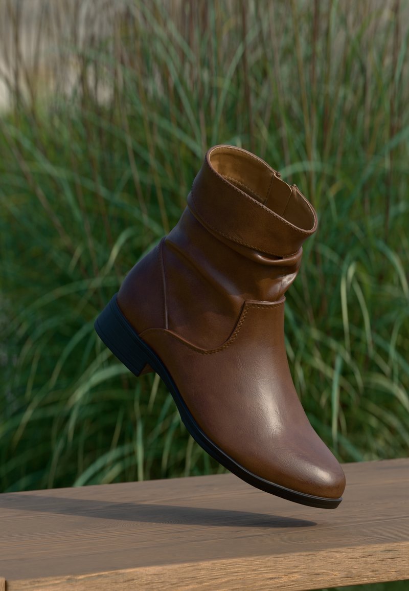 Bottine en cuir marron avec petit talon noir suspendue au-dessus d'une surface en bois, herbe verte floue en arrière-plan.