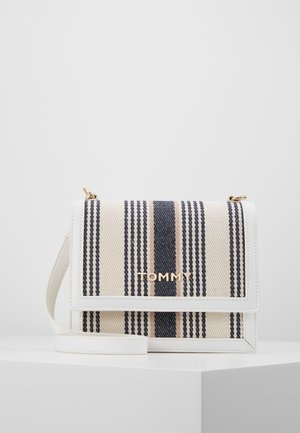 Petit sac bandoulière rectangulaire avec des bords blancs, des rayures verticales beige et marine, un logo doré "TOMMY" et une sangle blanche sur une surface blanche.