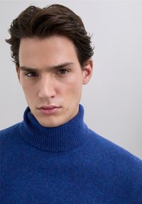 Maglione a collo alto in maglia blu con collo a coste; trama morbida e toni leggermente sfumati nel tessuto, design aderente.