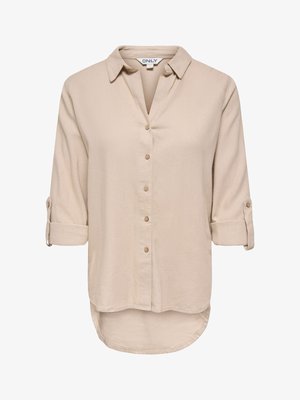 Chemisier beige à manches longues pour femme, avec poignets retroussés, boutonnage sur le devant, col et ourlet arrondi plus long à l'arrière.