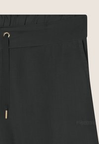 Pantalones negros con cintura elástica, cordón ajustable y herrajes en tono dorado. Presentan un sutil logo grabado en la tela.