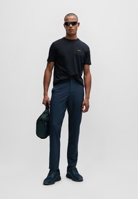 Camisa negra de manga corta con logo, pantalones ajustados azul marino y zapatillas negras; sosteniendo una bolsa negra. Tela suave, corte moderno, diseño minimalista.