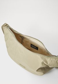 Borsa in tessuto riciclato verde oliva, con una texture liscia, chiusura con zip e tasca interna. Presenta un logo inciso in modo discreto sul davanti.