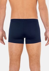 Tummansinisiä boxershortsit, jotka on valmistettu joustavasta kankaasta, jossa on elastinen vyötärönauha ja tiukka istuvuus, minimoidut saumat mukavuutta varten.