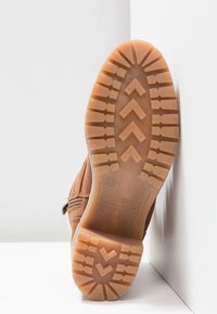 Bottine marron avec une tige en daim texturé, dotée d'une semelle en caoutchouc avec un motif de semelle en zigzag et un détail de fermeture éclair sur le côté.