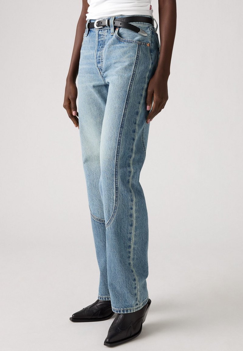 Jeans in denim azzurro chiaro con gamba dritta, cuciture a contrasto e un leggero effetto sbiadito. Abbinati a una cintura nera e scarpe con punta a contrasto.
