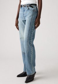 Blugi de denim albastru deschis cu croială dreaptă, detalii decolorate și cusături în contrast; asortați cu o centură neagră și cizme cu toc.