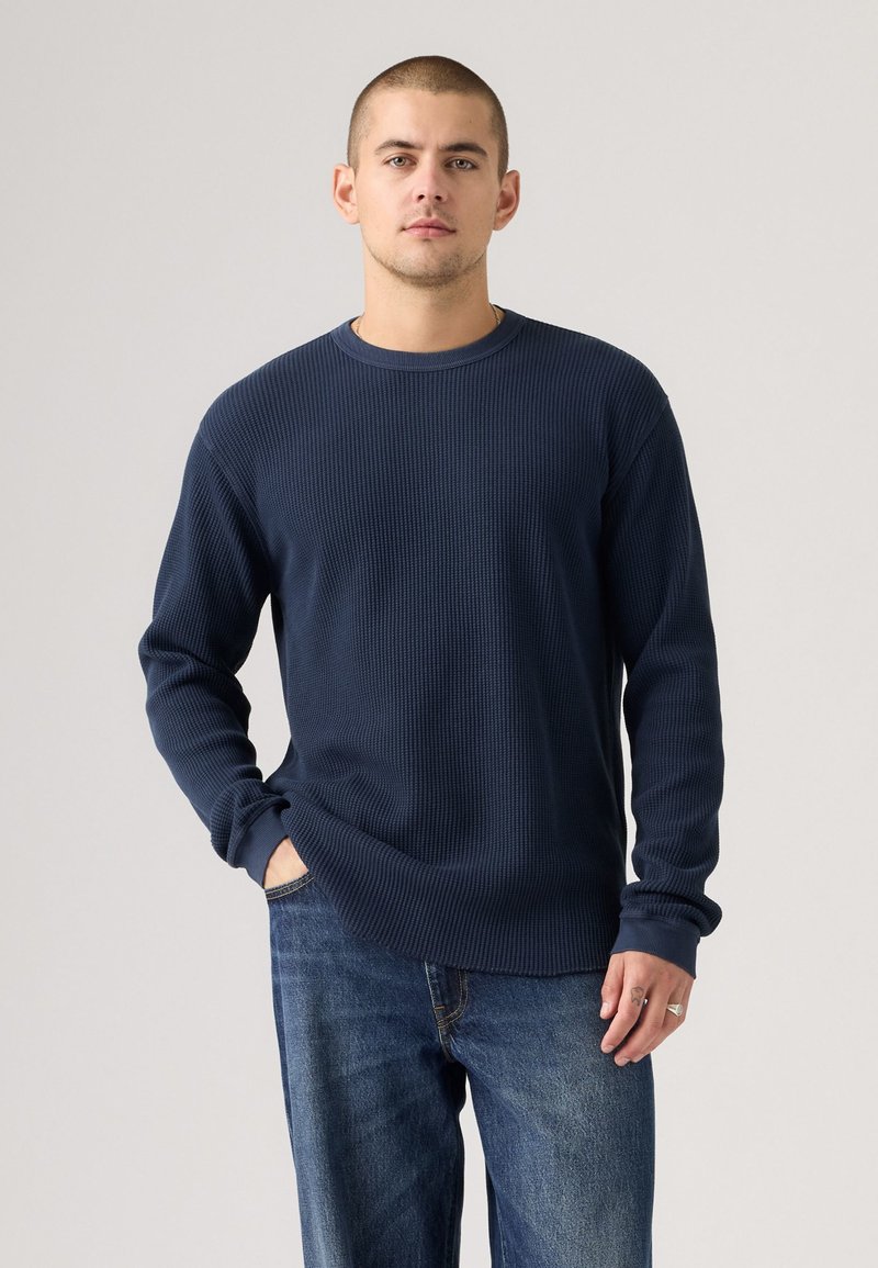 Marineblaues, geripptes Langarmshirt mit Rundhalsausschnitt, ausgestattet mit einem strukturierten Stoff und eng anliegenden Bündchen, kombiniert mit Jeans.