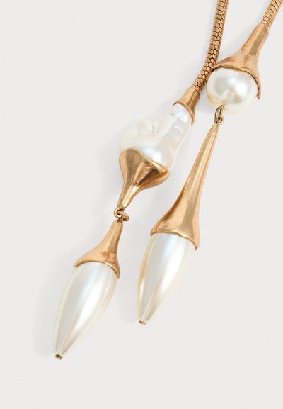 Collier en or et perles avec de grandes perles irrégulières et allongées serties dans des casquettes en or sur une chaîne en or texturée sur fond blanc.