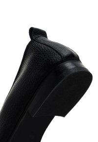 Zapato de cuero negro con una superficie texturizada, tacón bajo y punta redondeada. La parte trasera cuenta con un asa para facilitar su uso. La suela es lisa y plana.