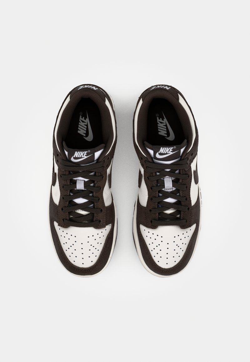 Sneakers in pelle marrone e bianca con punta perforata, lacci neri e logo Nike sulla linguetta. Upper liscio con un design atletico.
