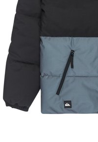 Čierna a �šedá prešívaná bunda s vnútorným vreckom na zips, elastickými manžetami a logom na prednej strane, s hladkou textúrou.