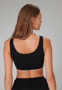 Reggiseno nero senza cuciture con spalline larghe e schiena a scollo, realizzato in tessuto morbido e elastico. Design semplice senza chiusure visibili o decorazioni.