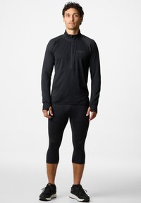 Zwarte sportieve lange mouwen top met een halflange rits kraag en gestructureerde mouwen, gecombineerd met zwarte driekwart leggings en zwarte sneakers.