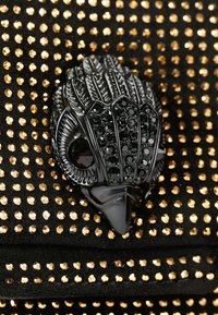 Zwart gestructureerd materiaal met gouden pailletten, met een gedetailleerd zwart accessoireontwerp dat op de voorkant lijkt op een hand.