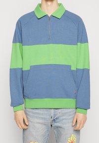 Sweat-shirt bleu et vert à col zippé, manches raglan, poche avant, et poignets et ourlet côtelés. Texture douce en coton.