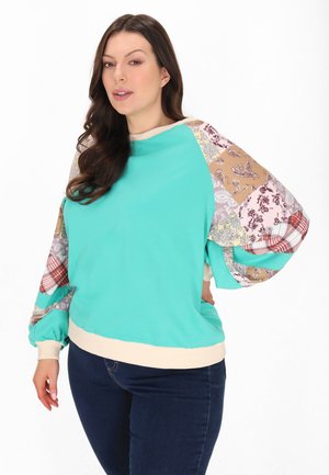 Türkiser Hoodie mit gemusterten, mehrfarbigen Ballonärmel und einem cremefarbenen Rippbund. Textil mit unterschiedlichen Strukturen.