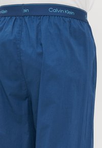 Uski blizu plave Calvin Klein bokserice s elastičnom trakom i logotipom na struku, nosi se s bijelom košuljom.