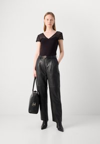 Top noir en V avec des manches en dentelle, associé à un pantalon en cuir taille haute. Des bottines noires et un sac à main structuré complètent le look.