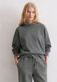 Szara bawełniana bluza z kapturem z troczkiem, luźny krój, ściągacze przy mankietach, w połączeniu z dopasowanymi szarymi spodniami dresowymi z bocznymi kieszeniami.