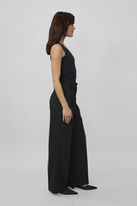 Black high-waisted wide-leg trousers with front pleats, paired with a fitted black tank top and pointed black shoes, side profile view.