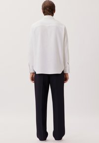 Witte lange mouwen shirt met een gestructureerde stof, rechte snit en een subtiele achterkant yoke detail; gecombineerd met donkere, wijde broekspijpen.