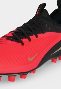 Κόκκινο και μαύρο ποδοσφαιρικό παπούτσι Nike με μαύρα κορδόνια, κόκκινες τάπες και μικρό χρυσό λογότυπο Nike στη πλευρά.