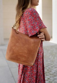 Hellbraune Leder-Umhängetasche mit glatter Oberfläche, ausgestattet mit einem einzelnen Riemen und einem kleinen, unten eingeprägten Logo.