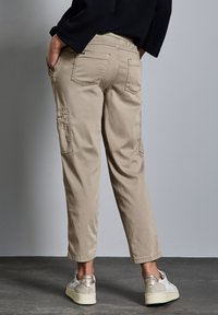Beige cargobroek met twee zijzakken, twee achterzakken, een taps toelopend ontwerp en een manchet bij de enkel, gecombineerd met witte sneakers.