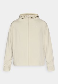 Világosbézs dzseki elülső cipzárral, állítható kapucnival és rugalmas mandzsettákkal. Sima tapintású, hálós béléssel. Minimalista kialakítás és logórészlet.