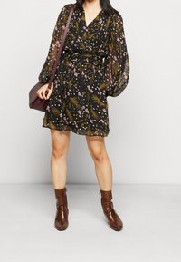 Černé květinové šaty s dlouhými, nabíranými rukávy a staženým pasem. Obsahují zelený a růžový květinový vzor. Doplněné hnědými kotníkovými botami.