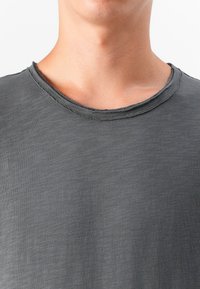 Primer plano del cuello y pecho de una persona con una camiseta de textura gris oscuro y cuello redondo. El fondo es liso y claro.