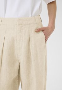 Beige linnen broeken met een geplooide voorkant, zijzakken en een relaxte pasvorm. De stof heeft een licht gestructureerde afwerking.