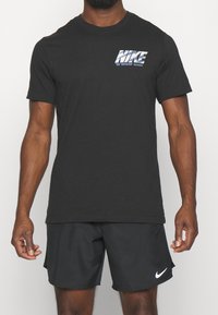 Černé bavlněné tričko s texturovaným stříbrným logem Nike. Design zahrnuje krátké rukávy a kulatý výstřih.