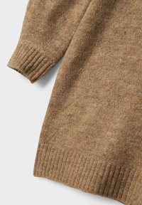 Manche et ourlet d'un pull en laine marron avec des bords côtelés sur un fond blanc.