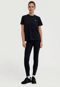 Zwart T-shirt met korte mouwen en een klein logo, gecombineerd met zwarte leggings met een gestructureerd patroon en zwarte sportschoenen.