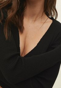 Black ribbed long-sleeve top with a deep V-neckline, featuring textured fabric and fitted sleeves, partially covering the arms.
