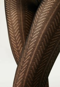 Collants noirs à motif géométrique avec des accents de tricot ouvert, mettant en valeur une surface texturée et une coupe ajustée.