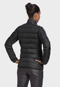 Chaqueta de abrigo negra con secciones acolchadas horizontales, cuello alto y mangas largas. Rayas blancas notables en los hombros. Textura suave.