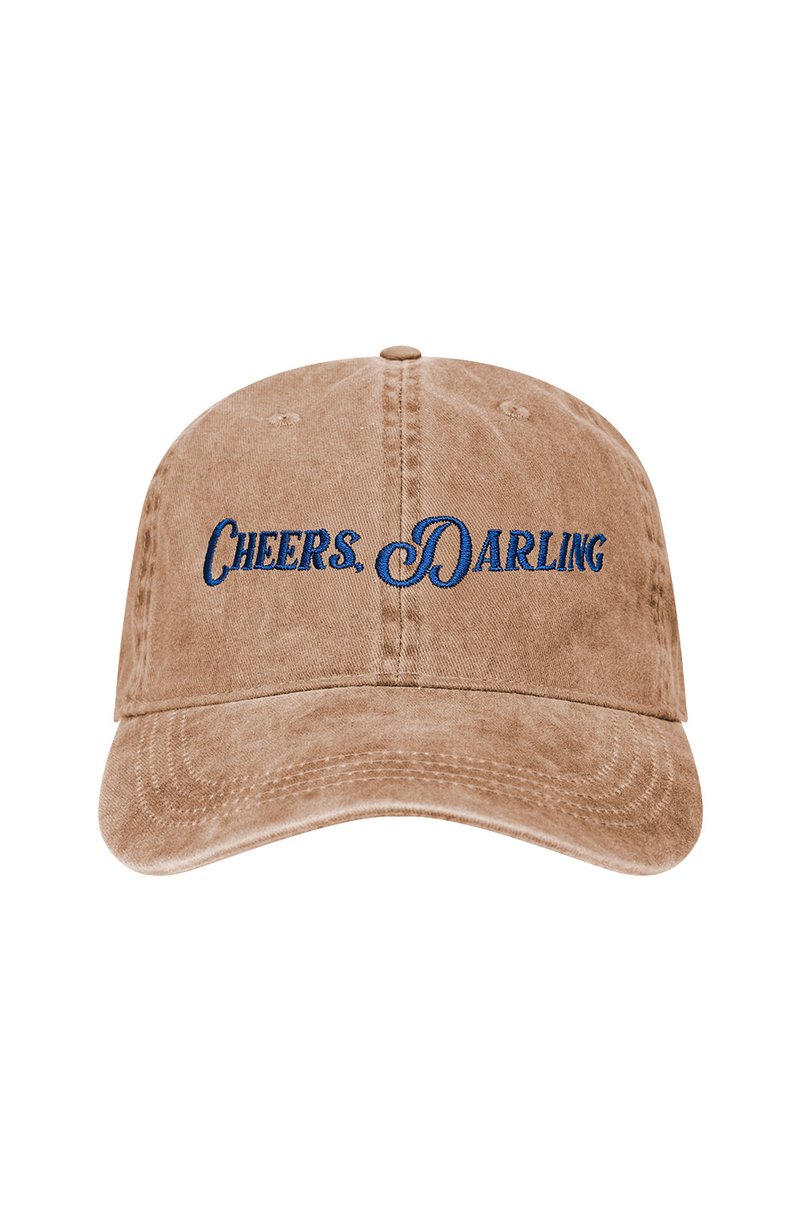 Beige Kappe mit gebogenem Schirm, versehen mit blauer gestickter Schrift "CHEERS. DARLING." und strukturiertem Stoff, entworfen für die Freizeit.