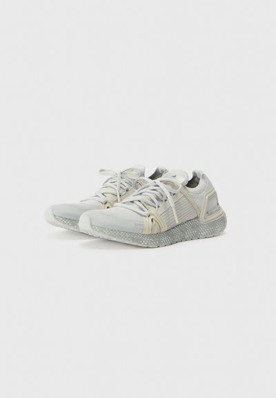 Light grey athletic shoes with a textured mesh upper, cream accents, and a speckled rubber sole. Features flat laces and a supportive design.