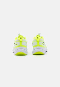 White athletic shoes with neon yellow accents, mesh panels, and a rounded toe. Features a pull tab on the heel and textured soles.