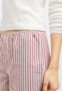 Lagana pamučna hlače s okomitim crvenim i bijelim prugama. Imaju elastični pojas i mali logotip u blizini kuka.