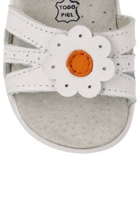 Sandal de cuero blanco con una embellishment en forma de flor con un centro naranja, plantilla de textura suave y diseño de múltiples correas.