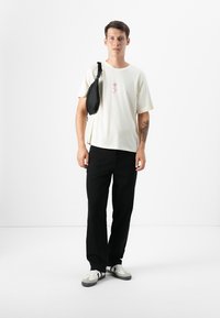 White short-sleeve t-shirt featuring a pink floral graphic, paired with black trousers. Accessory: black crossbody bag. Footwear: gray-white sneakers.