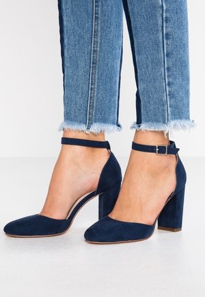 Navy suède hoge hakken met een spitse neus, enkelbandje en blokhak. G gedragen met blauw jeans met rafelige zoom.