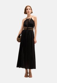 Czarna maxi sukienka z koronkowym górnym fasonem i regulowanymi ramiączkami, z talią podkreśloną i zwiewnym dołem. Akcesoria: pleciona kopertówka i sandały.
