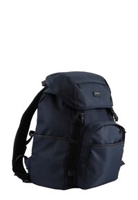Navy backpack made of durable fabric, featuring a roll-top closure, padded shoulder straps, multiple pockets, and textured accents.