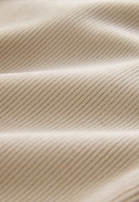 Gros plan sur un tissu beige avec une texture côtelée verticale fine créant de doux plis et des ombres.